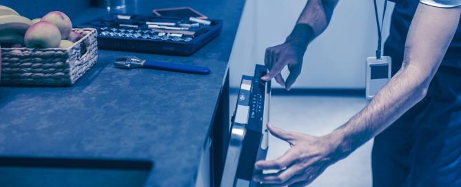 Mann Arbeitet an einer Spülmaschine in einer Küche, auf der Küche liegen Äpfel und sein Werkzeugkoffer