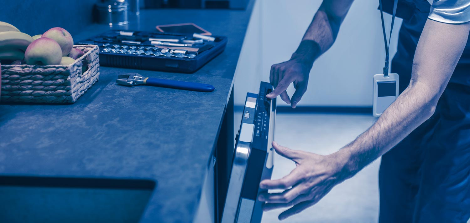 Mann Arbeitet an einer Spülmaschine in einer Küche, auf der Küche liegen Äpfel und sein Werkzeugkoffer